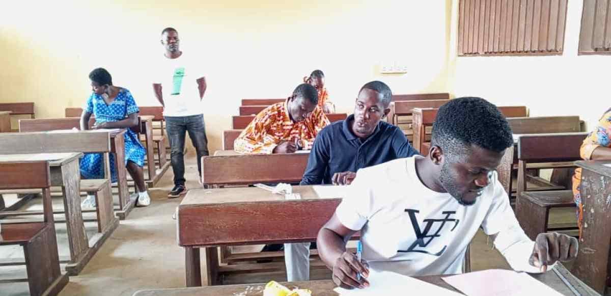Façade d'un lycée gabonais avec des élèves se dirigeant vers l'entrée pour composer un examen