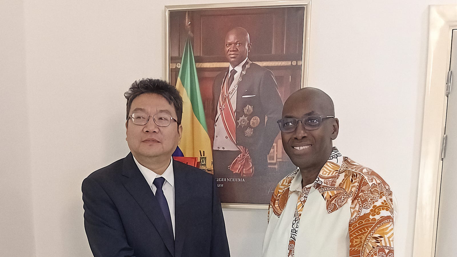 Rencontre diplomatique entre un responsable gabonais et un ambassadeur, drapeaux du Gabon et de la Chine en arrière-plan.