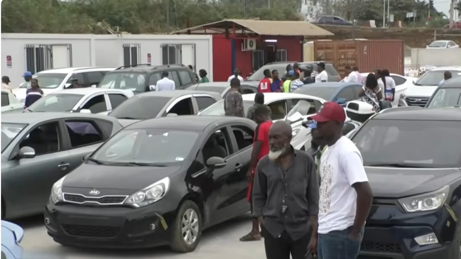 Véhicules alignés lors d'une vente aux enchères publique au Gabon, avec des visiteurs les inspectant