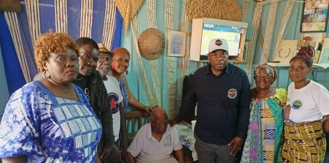 Un centenaire gabonais assis chez lui, entouré de membres d'une association venue lui remettre des produits de première nécessité.