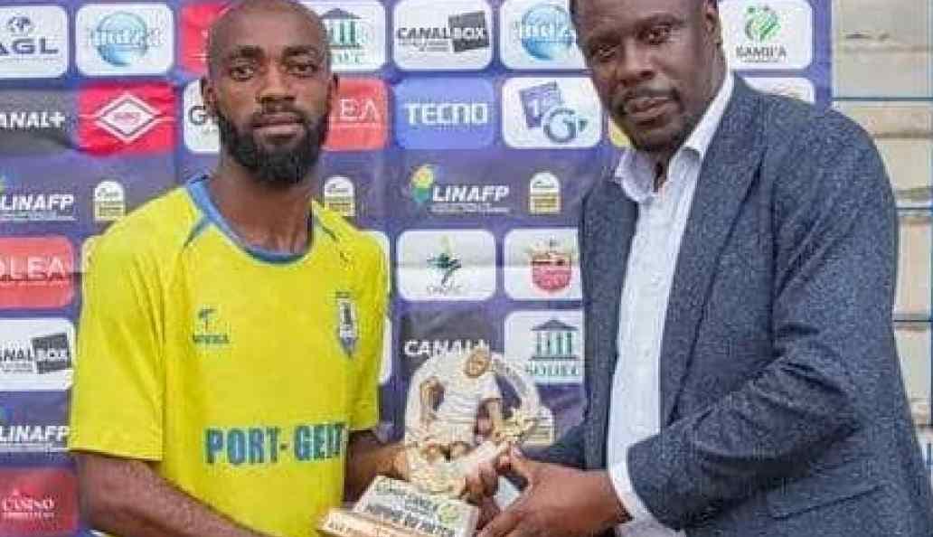 Joueur de football en maillot du Stade Mandji célébrant un but sur un terrain gabonais