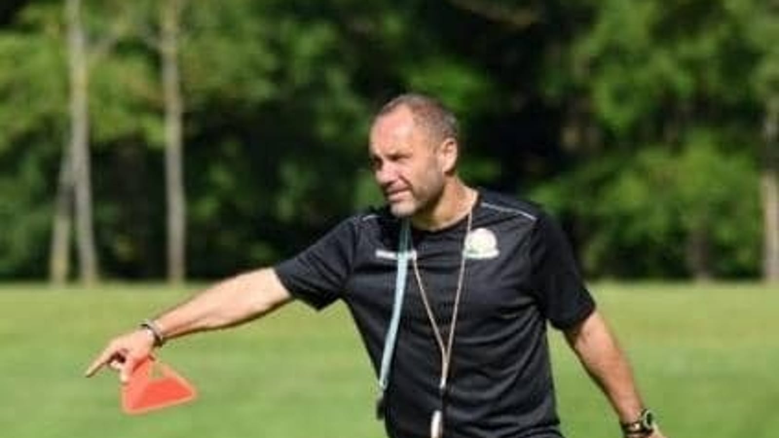 Un entraîneur de football se tient sur un terrain, en tenue de sport