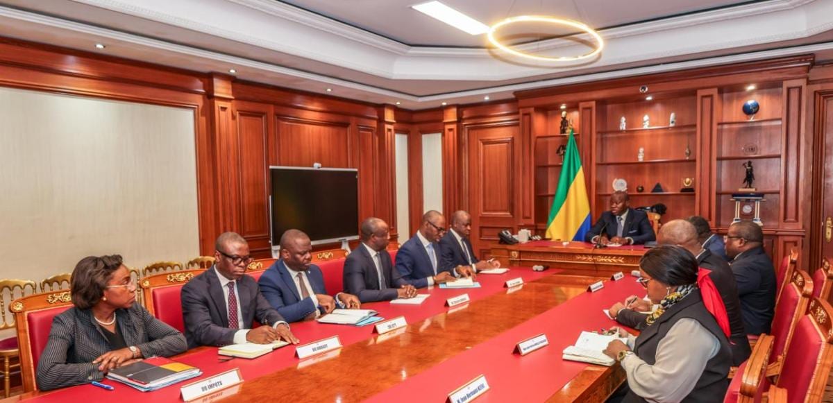 Réunion officielle autour d’une grande table avec drapeaux gabonais