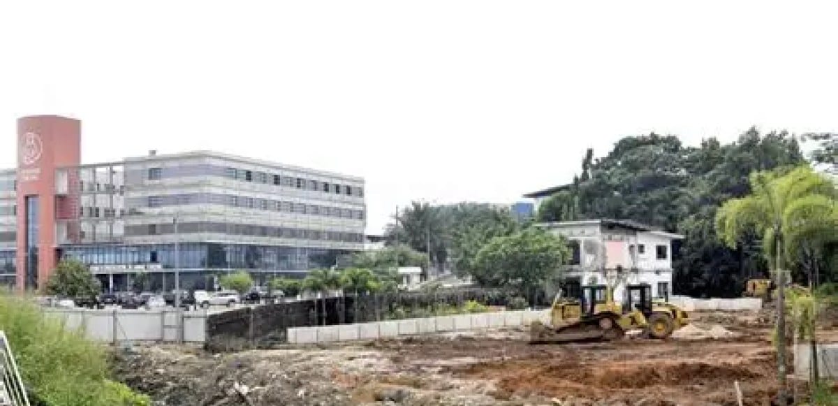 Quartier populaire gabonais avec habitations en tôle et engins de chantier au loin.