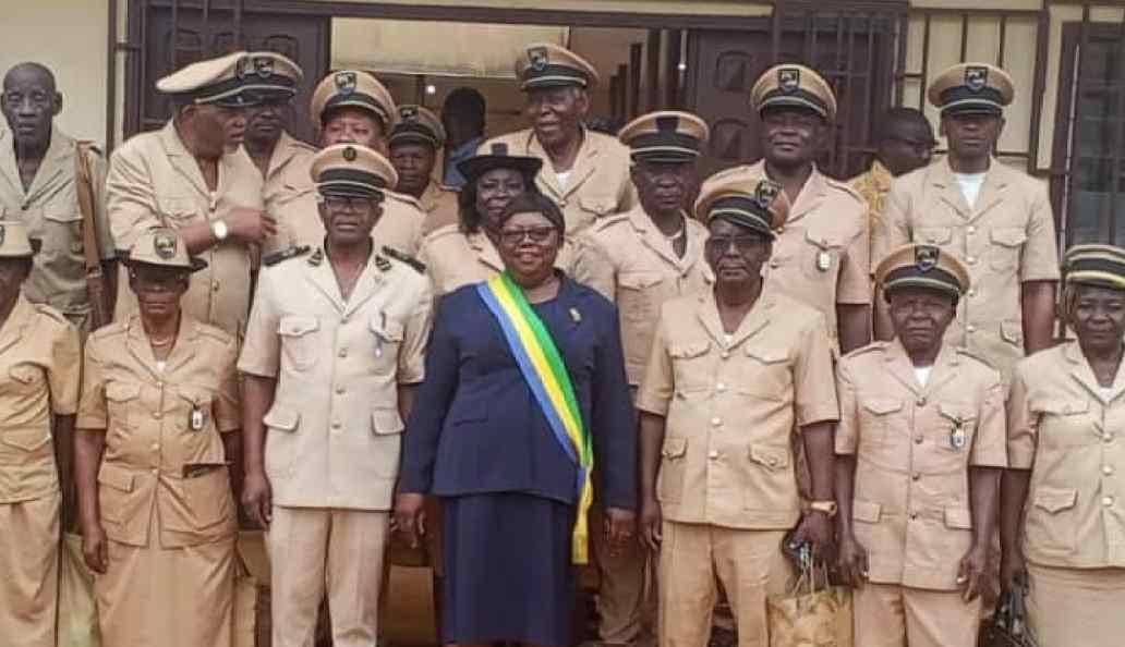 Une femme échangeant avec des responsables administratifs devant un bâtiment public à Ntoum, au Gabon.