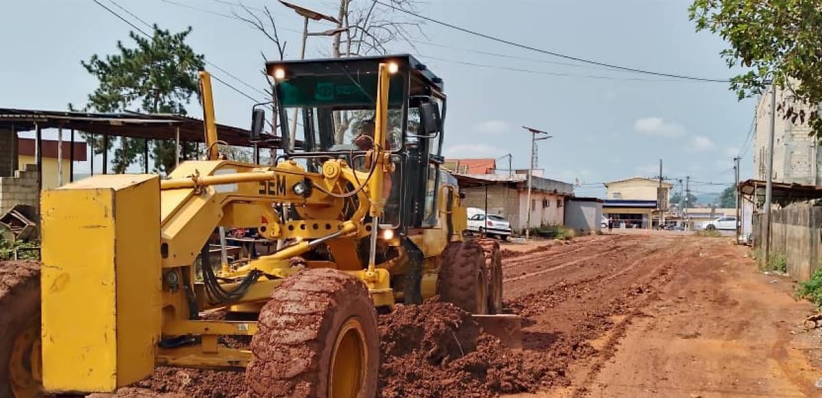 Engin de chantier reprofilant une route en terre dans un quartier de ville gabonaise