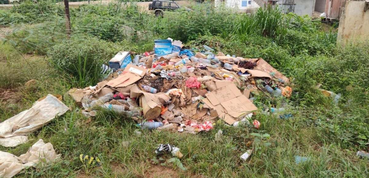 Nid-de-poule transformé en mare d'eau stagnante avec des déchets épars, en bord de route à Ndjolé.